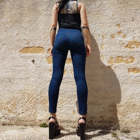 Donna che indossa slim jeggings blu, vista da dietro si vede effetto push-up, abbinati con top nero e scarpe con tacco per occasioni chic